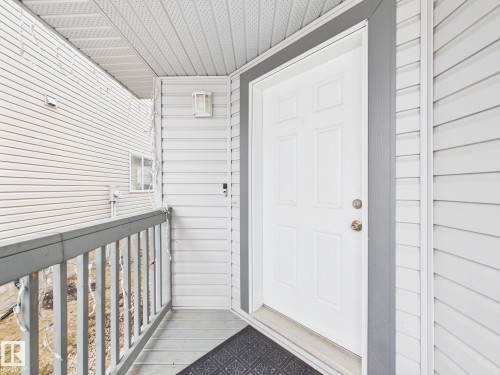 A covered entry with a white paneled door, light-colored siding, and a deck with grey railings - 9073 Scott Crescent, Edmonton, AB - Outdoor With Exterior