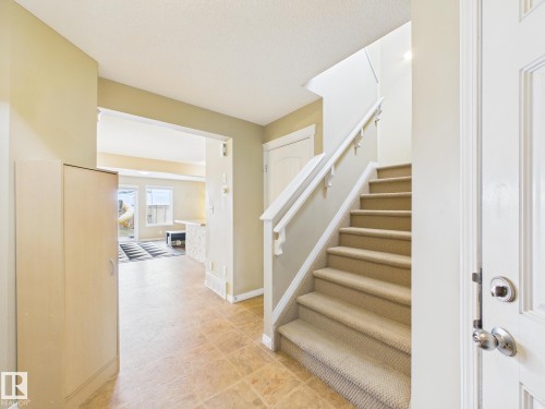 Entryway featuring tiled flooring, a carpeted staircase with a white railing, and a view into a living area with large windows - 9073 Scott Crescent, Edmonton, AB - Indoor Photo Showing Other Room