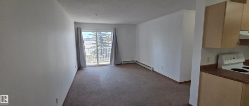 Spacious living area with carpeting, a sliding glass door leading to a balcony, and an open layout to the kitchen featuring light wood cabinetry - 208A 260 Spruce Ridge Road, Spruce Grove, AB - Indoor