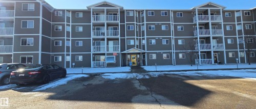 The property features a five-story building with balconies, a paved parking area, and a central entrance - 208A 260 Spruce Ridge Road, Spruce Grove, AB - Outdoor With Balcony With Facade