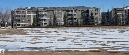 The property features a multi-story building with balconies, a dark-colored roof, and a light-colored exterior facade - 208A 260 Spruce Ridge Road, Spruce Grove, AB - Outdoor With Body Of Water