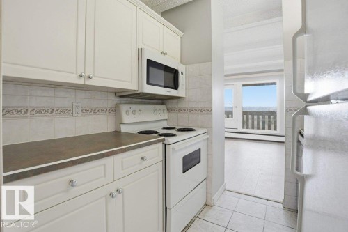The kitchen features white cabinetry, a tiled backsplash with a decorative border, and a white stove with an overhead microwave - 604 9918 101 Street, Edmonton, AB - Indoor Photo Showing Kitchen