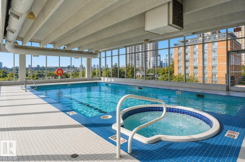 The property offers an indoor swimming pool with a hot tub, featuring large windows that provide abundant natural light and views of the surrounding urban landscape - 604 9918 101 Street, Edmonton, AB - Indoor Photo Showing Other Room With In Ground Pool