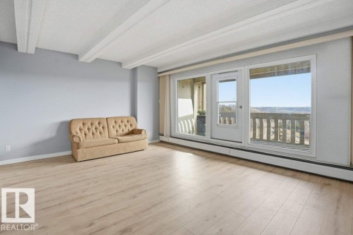 Living area featuring exposed ceiling beams, light wood-style flooring, and a sliding glass door leading to a balcony with views - 604 9918 101 Street, Edmonton, AB - Indoor