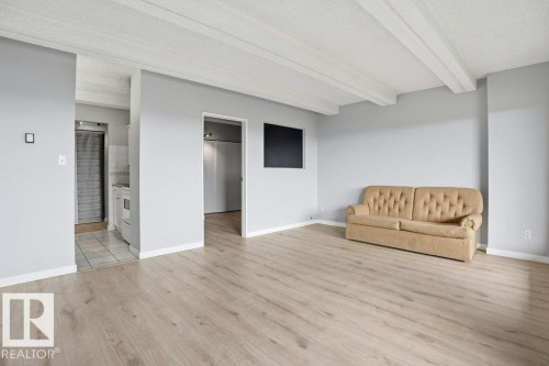 Spacious living area featuring light wood-style flooring, light grey walls, and a white beamed ceiling - 604 9918 101 Street, Edmonton, AB - Indoor