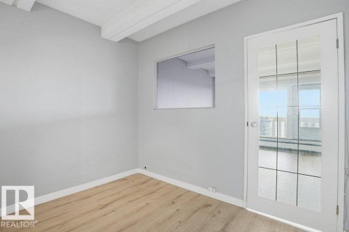 This room features light wood-style flooring, white baseboards, and a glass-paneled door - 604 9918 101 Street, Edmonton, AB - Indoor Photo Showing Other Room