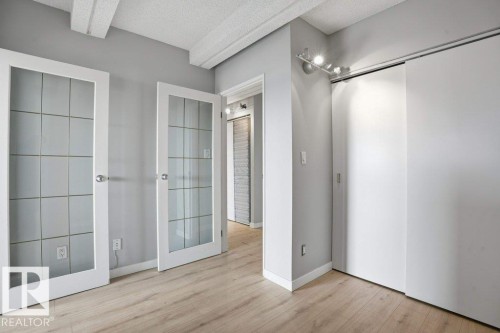 This room features two glass-paneled doors, light wood flooring, and a ceiling with exposed beams - 604 9918 101 Street, Edmonton, AB - Indoor Photo Showing Other Room