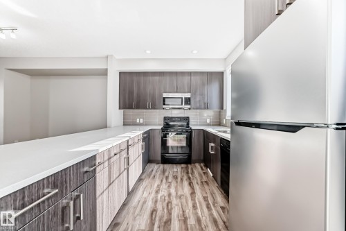The kitchen features dark wood-look cabinetry, a light-colored countertop, and stainless steel appliances, including a microwave, oven, and refrigerator - 75 2803 James Mowatt Trail, Edmonton, AB - Indoor Photo Showing Kitchen With Upgraded Kitchen