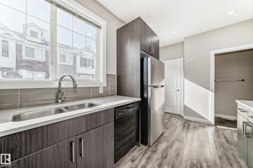The kitchen features a double basin stainless steel sink with a chrome faucet, light-colored countertops, dark wood cabinetry, and stainless steel appliances - 75 2803 James Mowatt Trail, Edmonton, AB - Indoor Photo Showing Kitchen With Double Sink