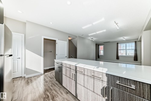The kitchen features a large island with a light-colored countertop and wood-grain cabinetry, complemented by stainless steel appliances - 75 2803 James Mowatt Trail, Edmonton, AB - Indoor