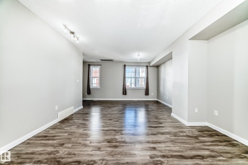 This open-concept living space features light gray walls, dark wood-style flooring, and white trim - 75 2803 James Mowatt Trail, Edmonton, AB - Indoor Photo Showing Other Room