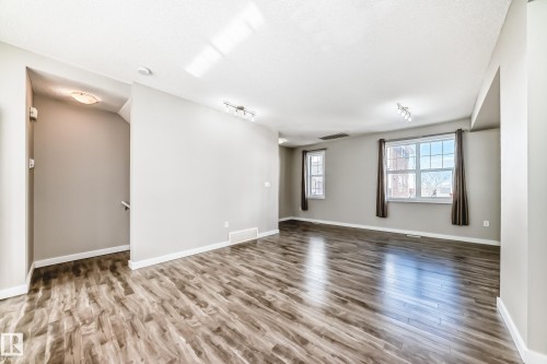 This bright interior features wood-look flooring, neutral wall colors, and windows with dark curtains - 75 2803 James Mowatt Trail, Edmonton, AB - Indoor Photo Showing Other Room