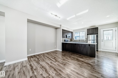 Open concept living space featuring light wood-style flooring and a kitchen with dark cabinetry, light countertops, and stainless steel appliances - 75 2803 James Mowatt Trail, Edmonton, AB - Indoor Photo Showing Kitchen