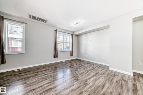 Spacious room featuring hardwood style flooring, light-colored walls, and two large windows with curtains - 75 2803 James Mowatt Trail, Edmonton, AB - Indoor Photo Showing Other Room