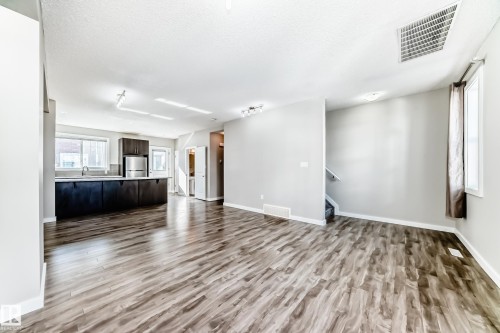 Spacious open concept living area featuring wood-look flooring and light-colored walls - 75 2803 James Mowatt Trail, Edmonton, AB - Indoor