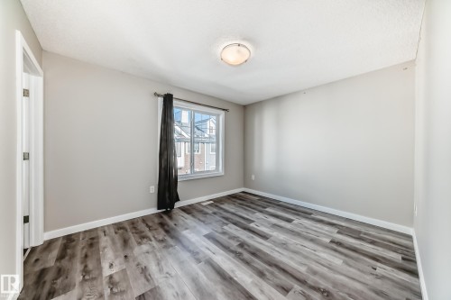 This room features light grey walls and multi-toned grey flooring - 75 2803 James Mowatt Trail, Edmonton, AB - Indoor Photo Showing Other Room
