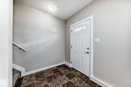 Entryway featuring a white paneled door with windowpanes, light gray walls, and patterned floor tiles - 75 2803 James Mowatt Trail, Edmonton, AB - Indoor Photo Showing Other Room