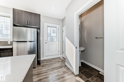 The kitchen features a stainless steel refrigerator, dark wood cabinetry, and a light-colored countertop - 75 2803 James Mowatt Trail, Edmonton, AB - Indoor Photo Showing Other Room