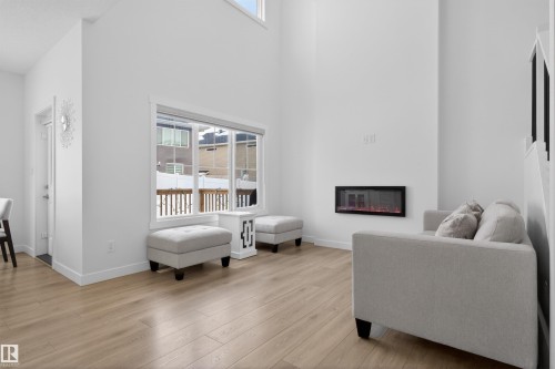 The living area features light-toned flooring, high ceilings, a large window, and an electric fireplace - 7344 177 Avenue, Edmonton, AB - Indoor With Fireplace