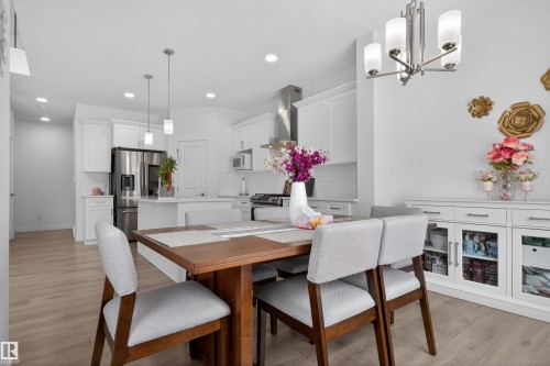 Open concept living area featuring a dining space with a contemporary chandelier, light wood flooring, and a kitchen with white cabinetry and stainless steel appliances - 7344 177 Avenue, Edmonton, AB - Indoor Photo Showing Dining Room
