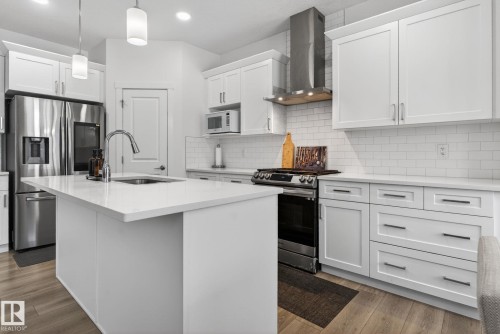 The kitchen features a large island with a sink, white cabinetry, stainless steel appliances, and light-colored flooring - 7344 177 Avenue, Edmonton, AB - Indoor Photo Showing Kitchen With Upgraded Kitchen