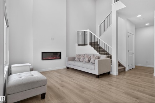 The living area features light-toned flooring, a wall-mounted fireplace, and a staircase with black metal railings - 7344 177 Avenue, Edmonton, AB - Indoor Photo Showing Living Room With Fireplace
