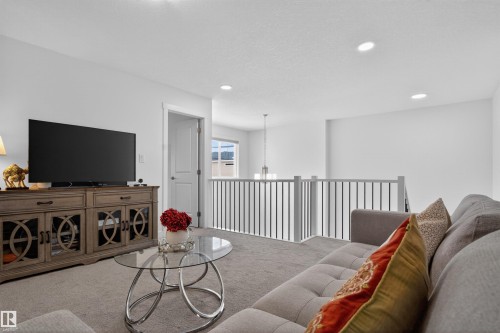 This living area features light-colored carpeting, recessed lighting, and a railing with dark vertical spindles - 7344 177 Avenue, Edmonton, AB - Indoor