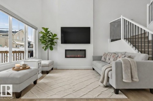 The living area features tall ceilings, large windows providing natural light, and an electric fireplace - 7344 177 Avenue, Edmonton, AB - Indoor Photo Showing Living Room With Fireplace
