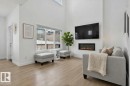 The living area features light-toned flooring, a wall-mounted fireplace, and large windows providing views of the exterior - 7344 177 Avenue, Edmonton, AB  - Indoor Photo Showing Living Room With Fireplace 