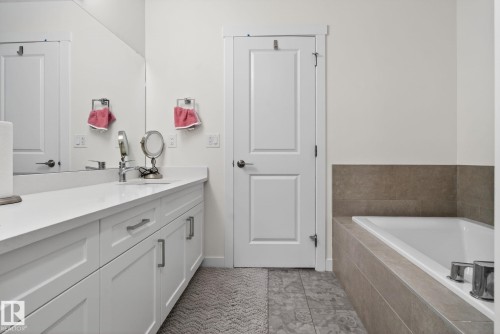 Bathroom featuring a vanity with a white countertop and white cabinetry, a large mirror, and a built-in bathtub with tiled surround - 7344 177 Avenue, Edmonton, AB - Indoor Photo Showing Bathroom