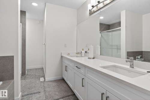 This bathroom features a double vanity with a white countertop and integrated sink, a large mirror, and a contemporary light fixture - 7344 177 Avenue, Edmonton, AB - Indoor Photo Showing Bathroom