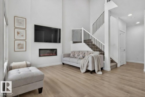 This inviting living space features high ceilings, light-toned flooring, and a modern fireplace for comfort - 7344 177 Avenue, Edmonton, AB - Indoor Photo Showing Other Room With Fireplace