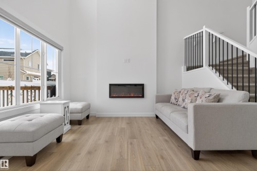 Living area featuring light wood flooring, a built-in electric fireplace, and large windows - 7344 177 Avenue, Edmonton, AB - Indoor Photo Showing Living Room With Fireplace