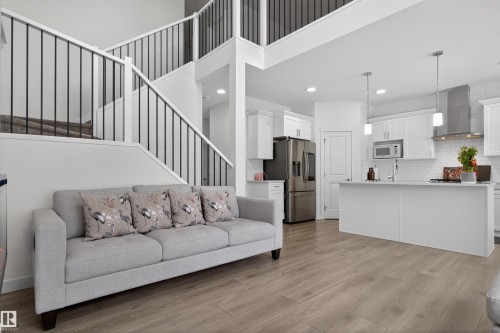 The property features an open-concept living space with light wood-style flooring, a kitchen with white cabinetry and stainless steel appliances, and a staircase with black metal balusters - 7344 177 Avenue, Edmonton, AB - Indoor Photo Showing Kitchen With Upgraded Kitchen