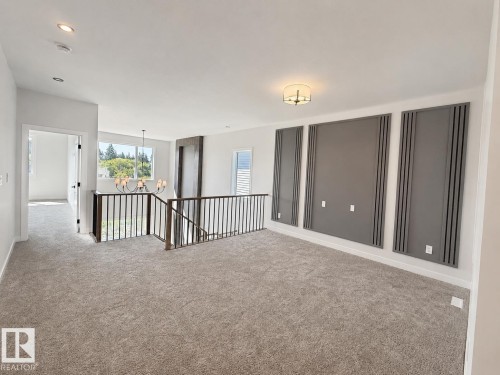 Expansive carpeted area featuring a prominent staircase with dark metal railings, a contemporary chandelier, recessed lighting, and decorative wall panels - 22 Meadowgrove Landing, Spruce Grove, AB - Indoor Photo Showing Other Room