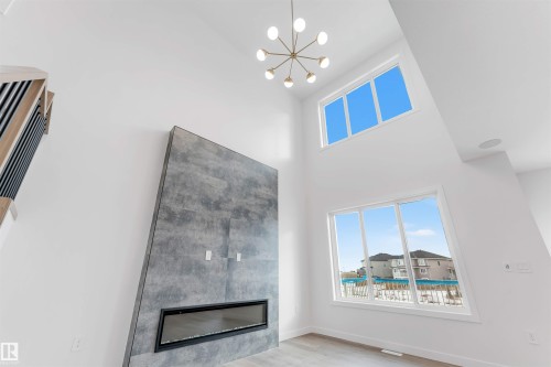 This living space features a modern linear fireplace set into a textured wall, high ceilings, and large windows providing ample natural light - 22 Meadowgrove Landing, Spruce Grove, AB - Indoor With Fireplace