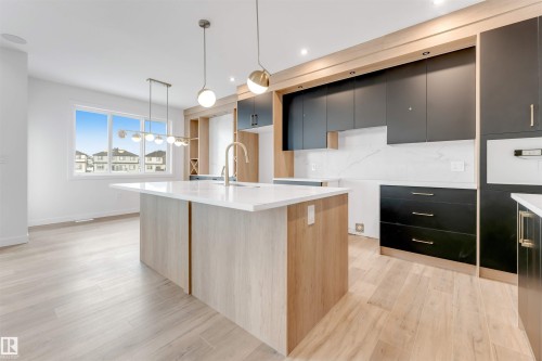 The kitchen features a large island with a light-toned wood finish and a white countertop, modern pendant lighting, and light wood flooring - 22 Meadowgrove Landing, Spruce Grove, AB - Indoor Photo Showing Kitchen With Upgraded Kitchen
