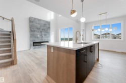The property features light-colored hardwood flooring, a contemporary kitchen island with a white countertop, and a built-in fireplace with a stone-textured wall - 