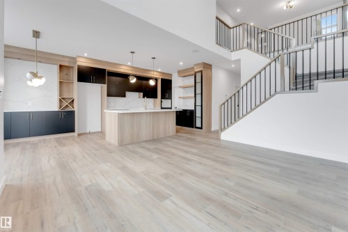Open concept living area with light wood-style flooring, a modern kitchen island, and a prominent staircase featuring dark metal balusters - 22 Meadowgrove Landing, Spruce Grove, AB - Indoor Photo Showing Kitchen
