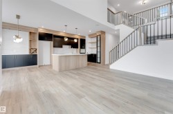Open concept living area with light wood-style flooring, a modern kitchen island, and a prominent staircase featuring dark metal balusters - 