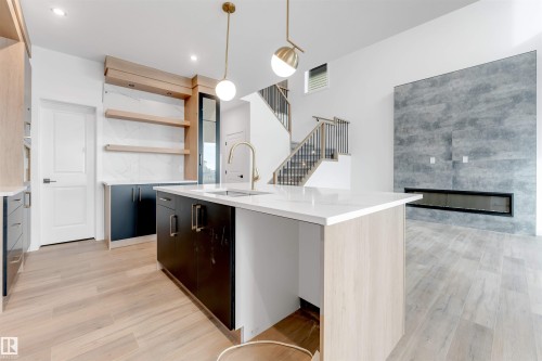 This open-concept living space features light wood-look flooring, a kitchen island with a white countertop, and a modern fireplace with a large gray tile surround - 22 Meadowgrove Landing, Spruce Grove, AB - Indoor Photo Showing Kitchen With Upgraded Kitchen