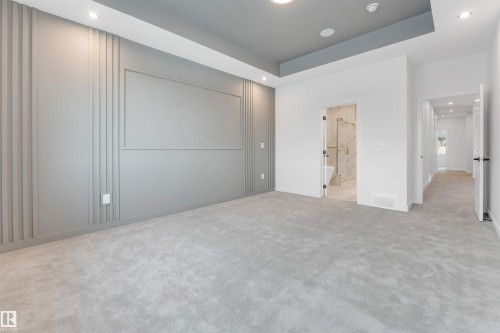 This expansive room features plush grey carpeting, a tray ceiling with recessed lighting, and a grey accent wall with decorative paneling - 22 Meadowgrove Landing, Spruce Grove, AB - Indoor Photo Showing Other Room
