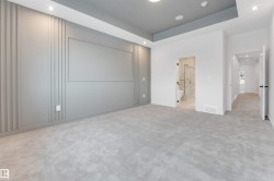 This expansive room features plush grey carpeting, a tray ceiling with recessed lighting, and a grey accent wall with decorative paneling - 