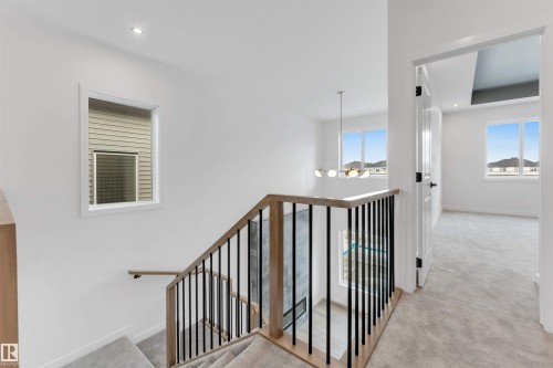 The property features a staircase with light wood handrails and black metal balusters, and a light-colored carpeted floor - 22 Meadowgrove Landing, Spruce Grove, AB - Indoor Photo Showing Other Room