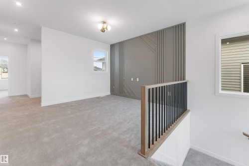 This room features light grey carpeting, recessed lighting, and a decorative accent wall with vertical and diagonal paneling - 22 Meadowgrove Landing, Spruce Grove, AB - Indoor Photo Showing Other Room