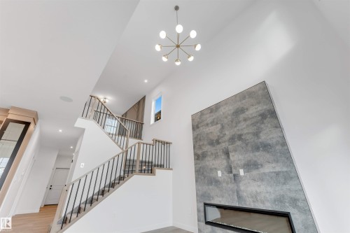 The property features a modern chandelier, a prominent staircase with dark metal balusters and light wood handrails, and a striking floor-to-ceiling fireplace with a linear insert - 22 Meadowgrove Landing, Spruce Grove, AB - Indoor Photo Showing Other Room
