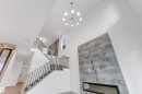 The property features a modern chandelier, a prominent staircase with dark metal balusters and light wood handrails, and a striking floor-to-ceiling fireplace with a linear insert - 22 Meadowgrove Landing, Spruce Grove, AB  - Indoor Photo Showing Other Room 