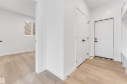 Hallway featuring light-colored flooring, white walls, and white doors with dark hardware - 