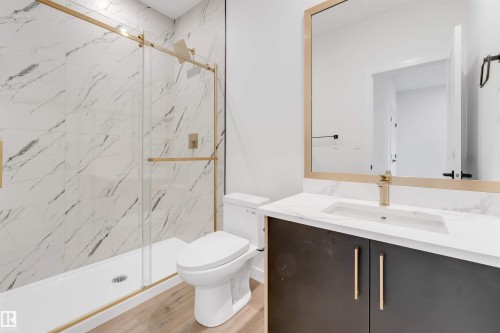The bathroom features a modern vanity with a white countertop and gold-toned fixtures, complemented by a shower with a sliding glass door and marble-patterned tiling - 22 Meadowgrove Landing, Spruce Grove, AB - Indoor Photo Showing Bathroom