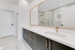 The bathroom features a double vanity with dark cabinetry, white countertops, and gold-toned hardware and faucets - 